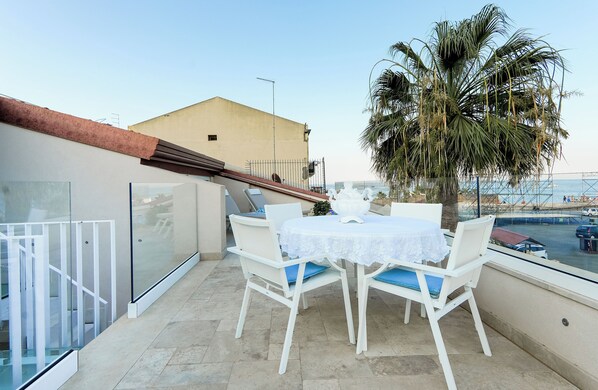 En balkon med et bord og stole, et palmetræ og havudsigt.
