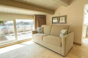 Ein Wohnzimmer mit einem beigefarbenen Sofa, zwei gerahmten Bildern an der Wand und Blick auf die Marina durch große Glaswände.