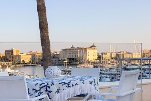 Une table recouverte d’une nappe blanche, agrémentée d’un vase décoratif, donnant sur une marina où l’on aperçoit des bateaux et des bâtiments en arrière-plan.