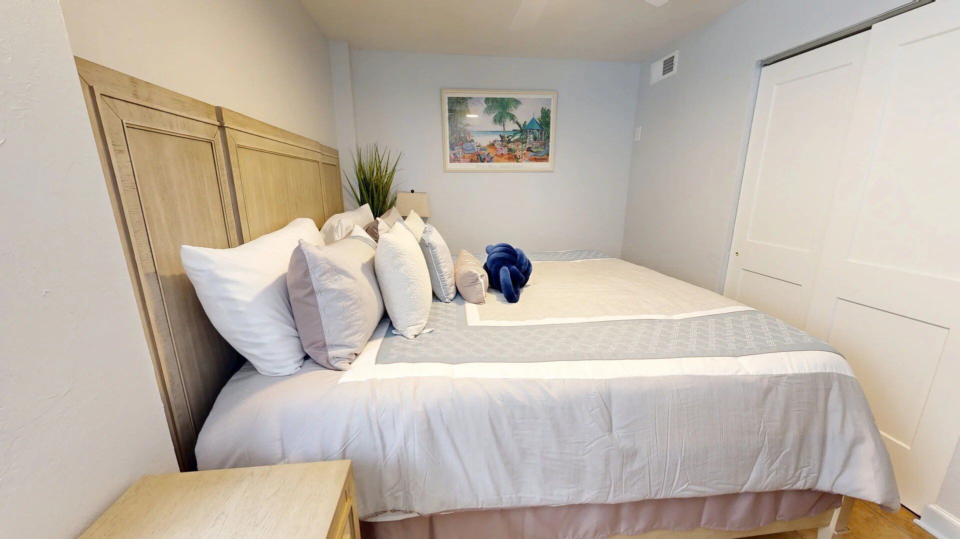Ein ordentlich eingerichtetes Schlafzimmer mit einem Bett, Kissen, einem blauen Plüschtier und einem gerahmten Bild an der Wand.