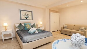A bedroom with a bed, bedside tables, a nightstand, a sofa, a decorative vase, and a wardrobe. - Marina Homes Elegant designroom1 Ortigiapartments (Syracuse)