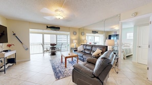 A living room with a sofa, a coffee table, a TV, and a balcony with a view. - Crescent Arms Vacation Rentals 703N Siesta Key Florida (Sarasota)