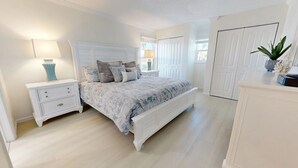 Een slaapkamer met een bed, nachtkastjes, een dressoir en een deur.