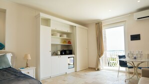 Ein Schlafzimmer mit Bett, Nachttisch, Schreibtisch, einer Küchenzeile und einem Balkon mit Blick.