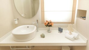Ein Badezimmer mit einem weißen Waschbecken, einem Spiegel, einer Vase mit Blumen und einem Handtuchhalter.