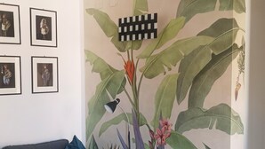 Olohuone, jossa on harmaa sohva, musta lattiavalaisin ja seinä, jossa on suuri kasvitaiuluinen seinämaalaus.