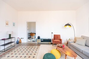 A modern living room with a sofa, coffee table, and a lamp. There is a chair and a small table with a vase and a lamp. The room has a patterned rug and a door leading to another room. - Casa Charlotte by Ortigia Apartments (Syracuse)