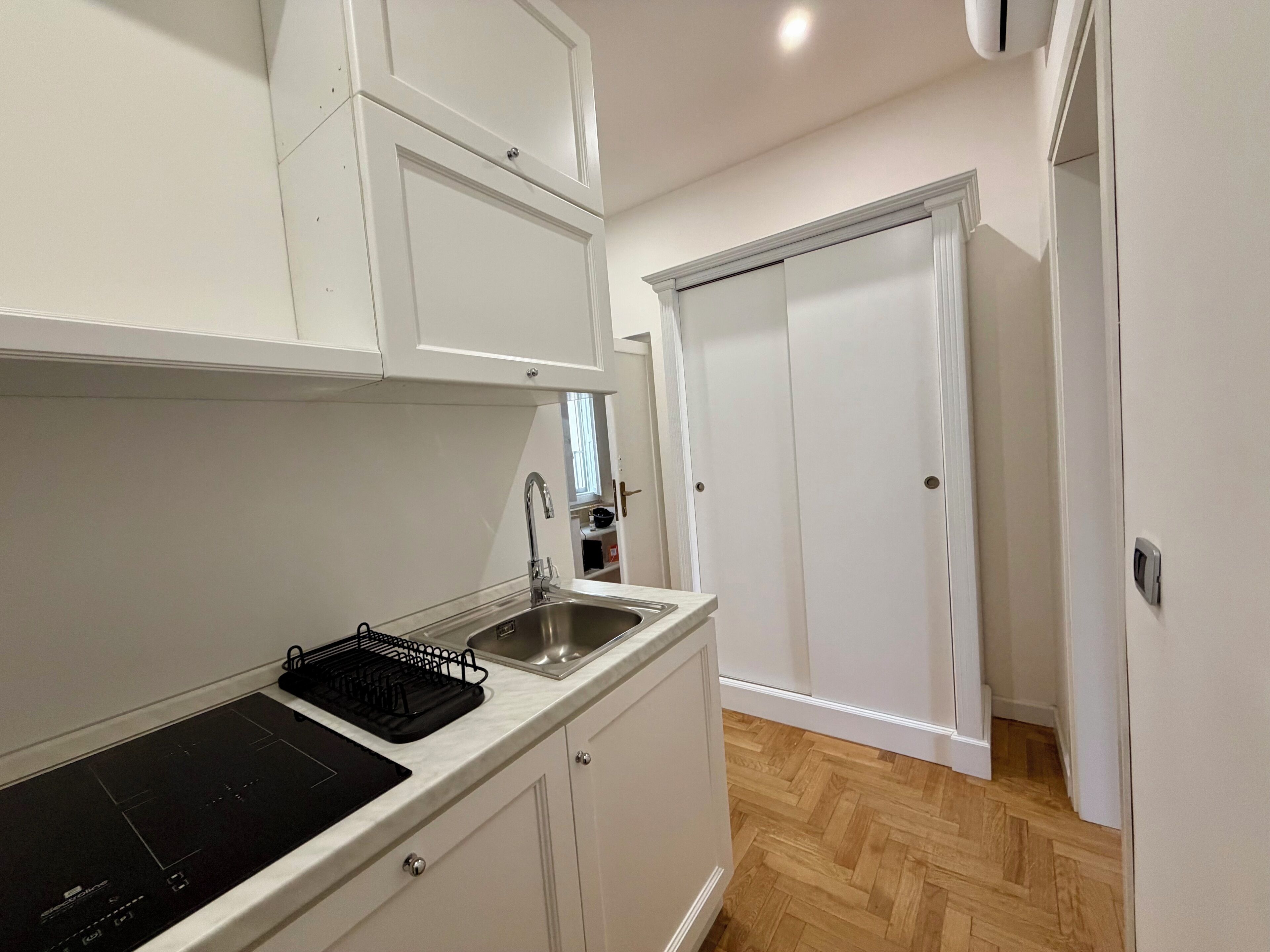 A compact kitchen with white cabinetry, a stainless steel sink, and a black induction cooktop.