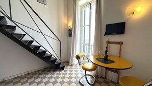 Una habitación con piso a cuadros, una escalera, una mesa con dos vasos, una silla y un televisor en la pared.