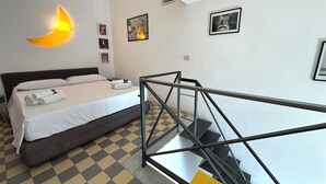 Una habitación de hotel con una cama, una lámpara de pared en forma de luna creciente, una escalera y un suelo a cuadros.