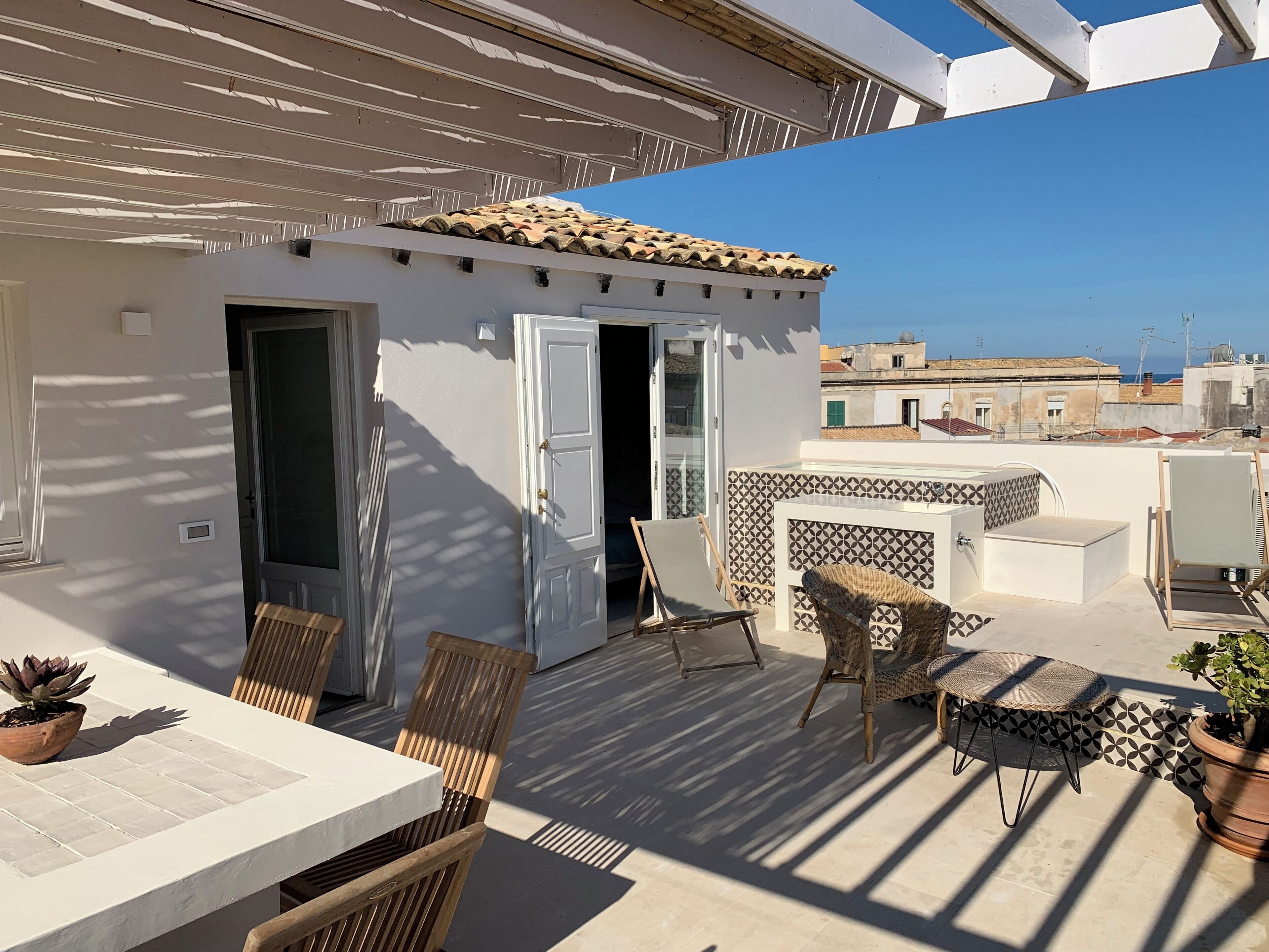 A rooftop terrace with a white wall, a tiled roof, and a view of the cityscape.