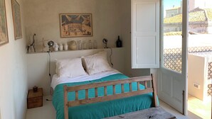 A bedroom with a wooden bed, a white door, a balcony with a tiled floor, and a painting on the wall. - Terrazza Cavalieri di Malta by Ortigiapartments (Syracuse)
