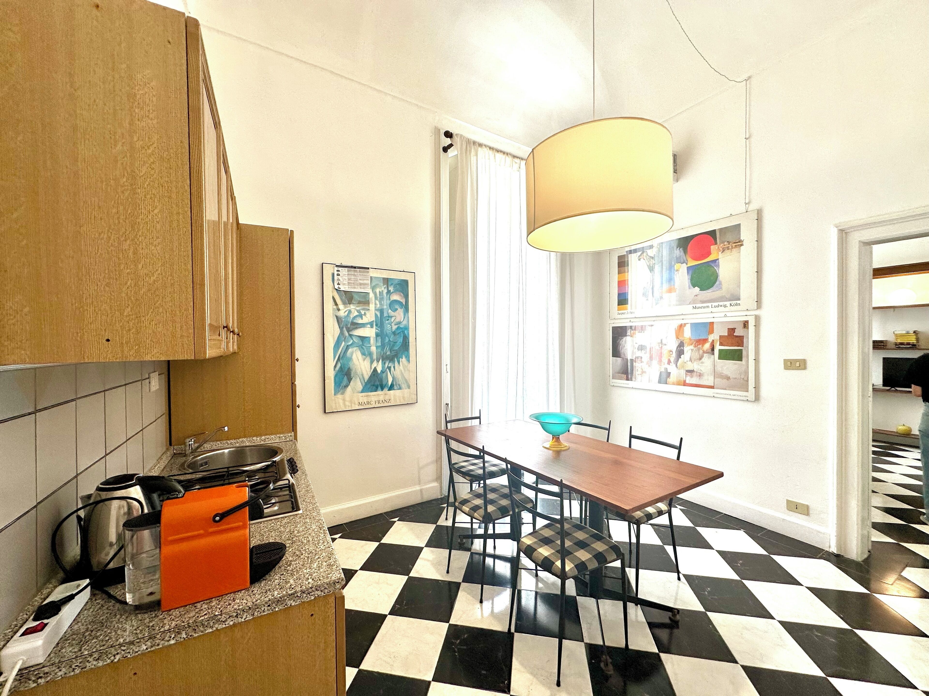 A kitchen with a checkered floor, a dining table with chairs, and a hanging lamp.