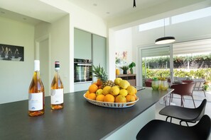 A modern kitchen with a fruit bowl, two bottles of wine, and a dining area with chairs and a table. - Villa Alice by Ortigiaapartments (Syracuse)