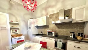 Una cocina moderna con armarios blancos, una mesa de vidrio, microondas, estufa y una lámpara de araña roja.