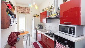 A compact kitchen with red cabinets, a white countertop, a microwave, a stove, and a refrigerator. - Poseidone Apartment - Two Bedroom Apartment, Sleeps 4 (Syracuse)