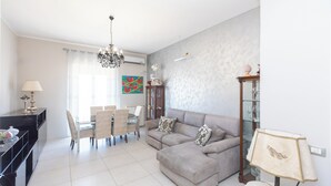 A modern living room with a sofa, dining table, chairs, and a chandelier. - Poseidone Apartment - Two Bedroom Apartment, Sleeps 4 (Syracuse)