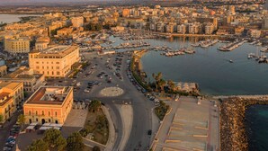 An aerial view of a coastal city with a marina, buildings, and roads. - Lucea Sea Terrace by Ortigiapartments (Syracuse)