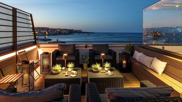 A rooftop terrace with wicker furniture, potted plants, and a view of the sea and cityscape. - Lucea Sea Terrace by Ortigiapartments (Syracuse)