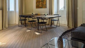 A spacious room with a dining table, chairs, a hanging light fixture, and a large window. - Lucea Sea Terrace by Ortigiapartments (Syracuse)
