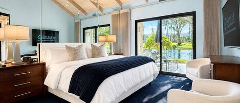 A hotel room with a large bed, a desk, a chair, and a view of a pool and greenery.