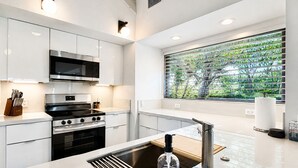 Una cocina moderna con electrodomésticos de acero inoxidable, un amplio ventanal con vistas a zonas verdes y una isla central con fregadero y una botella de lavavajillas.