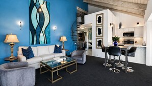 Una sala de estar moderna con una pared azul destacada, una mesa de centro de vidrio y un comedor con taburetes de bar.