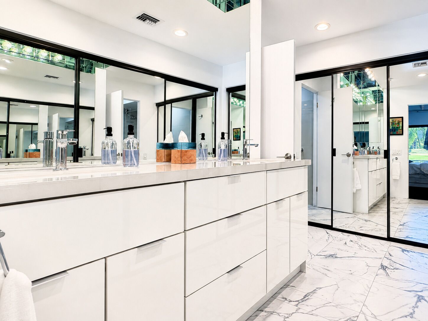 A modern bathroom with a large mirror, a marble floor, and a glass door leading to a shower area.
