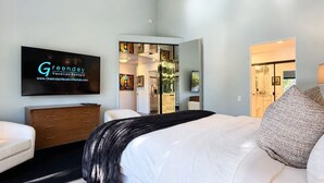 Habitación de hotel moderna con una cama grande, un televisor de pantalla plana en la pared, un aparador de madera y un vestidor con espejo.