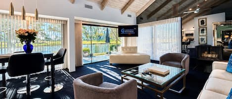 Una sala de estar moderna con techo alto, chimenea y un amplio ventanal con vista al agua.