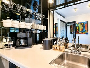 A modern kitchen with a large island, coffee machines, and a variety of kitchenware. - Sunset Serenade: Inspiring Views, Modern Desert Sanctuary...managed by Greenday! (Rancho Mirage)
