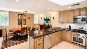 A modern kitchen with wooden cabinets, a stainless steel stove, and a dining area with a rug. - Harvard Hideaway: sun-splashed, westerly views in The Springs Country Club. Managed by Greenday! (Rancho Mirage)