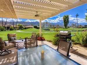 An outdoor patio with a glass table, chairs, a grill, and a view of a golf course and mountains. - Harvard Hideaway: sun-splashed, westerly views in The Springs Country Club. Managed by Greenday! (Rancho Mirage)