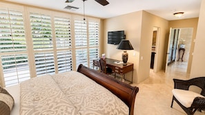 A bedroom with a large bed, a desk with a lamp, a television, and a chair. - Harvard Hideaway: sun-splashed, westerly views in The Springs Country Club. Managed by Greenday! (Rancho Mirage)