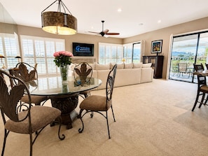 A spacious living room with a round glass table, a sofa, and a television mounted on the wall. - Harvard Hideaway: sun-splashed, westerly views in The Springs Country Club. Managed by Greenday! (Rancho Mirage)