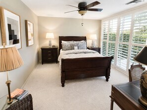 A bedroom with a bed, two bedside tables, a ceiling fan, and a large window with blinds. - Harvard Hideaway: sun-splashed, westerly views in The Springs Country Club. Managed by Greenday! (Rancho Mirage)