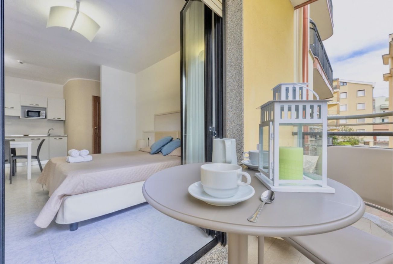 A hotel room with a bed, a small kitchenette, a dining area, and a balcony with a table and a lantern.