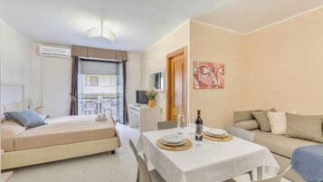 Una camera d'albergo moderna con un letto, un tavolo da pranzo per due persone, un divano e un balcone con tavolo e sedie.