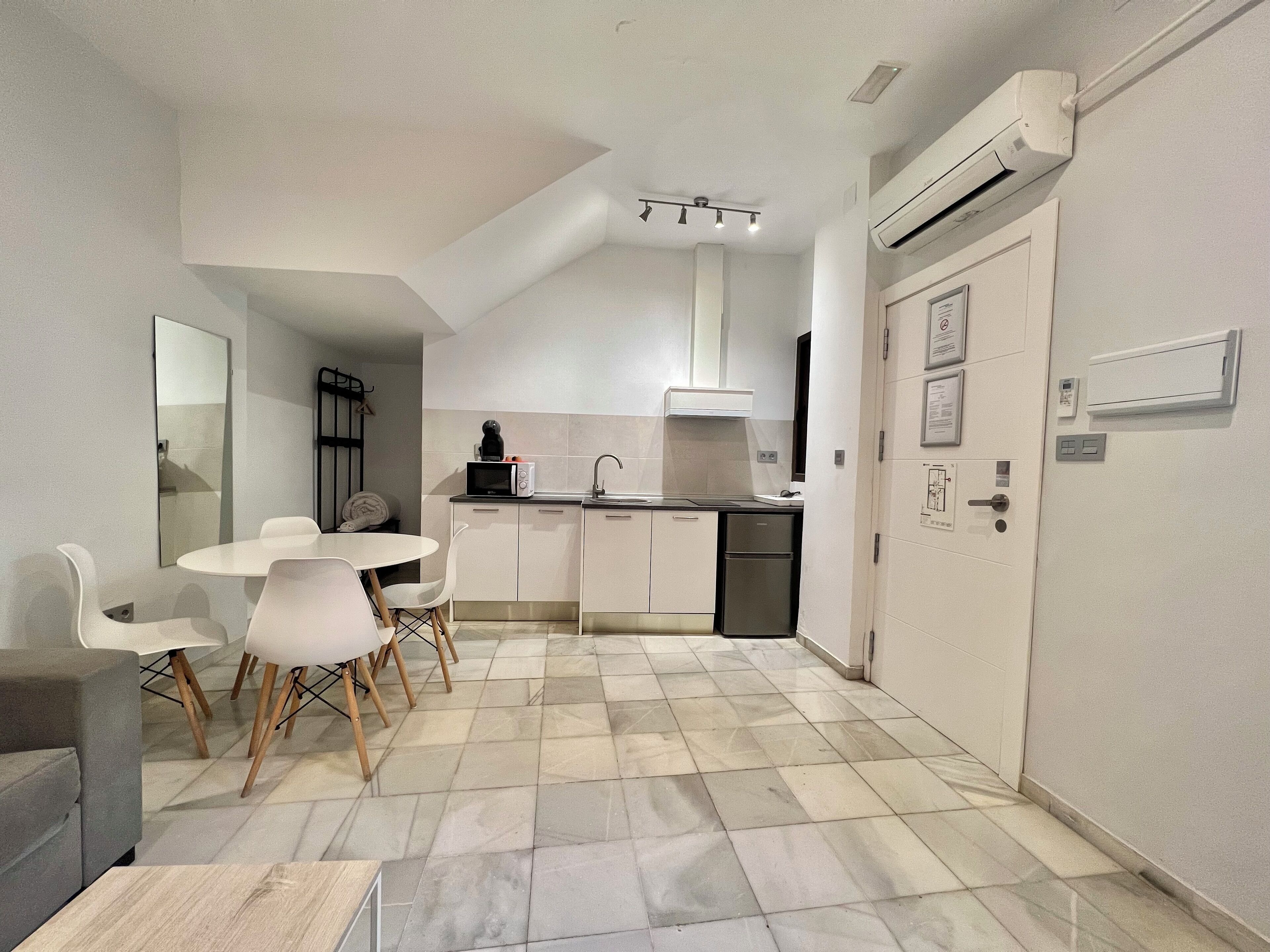 Una cocina compacta con armarios blancos, microondas y pileta. Hay un comedor con mesa y sillas.