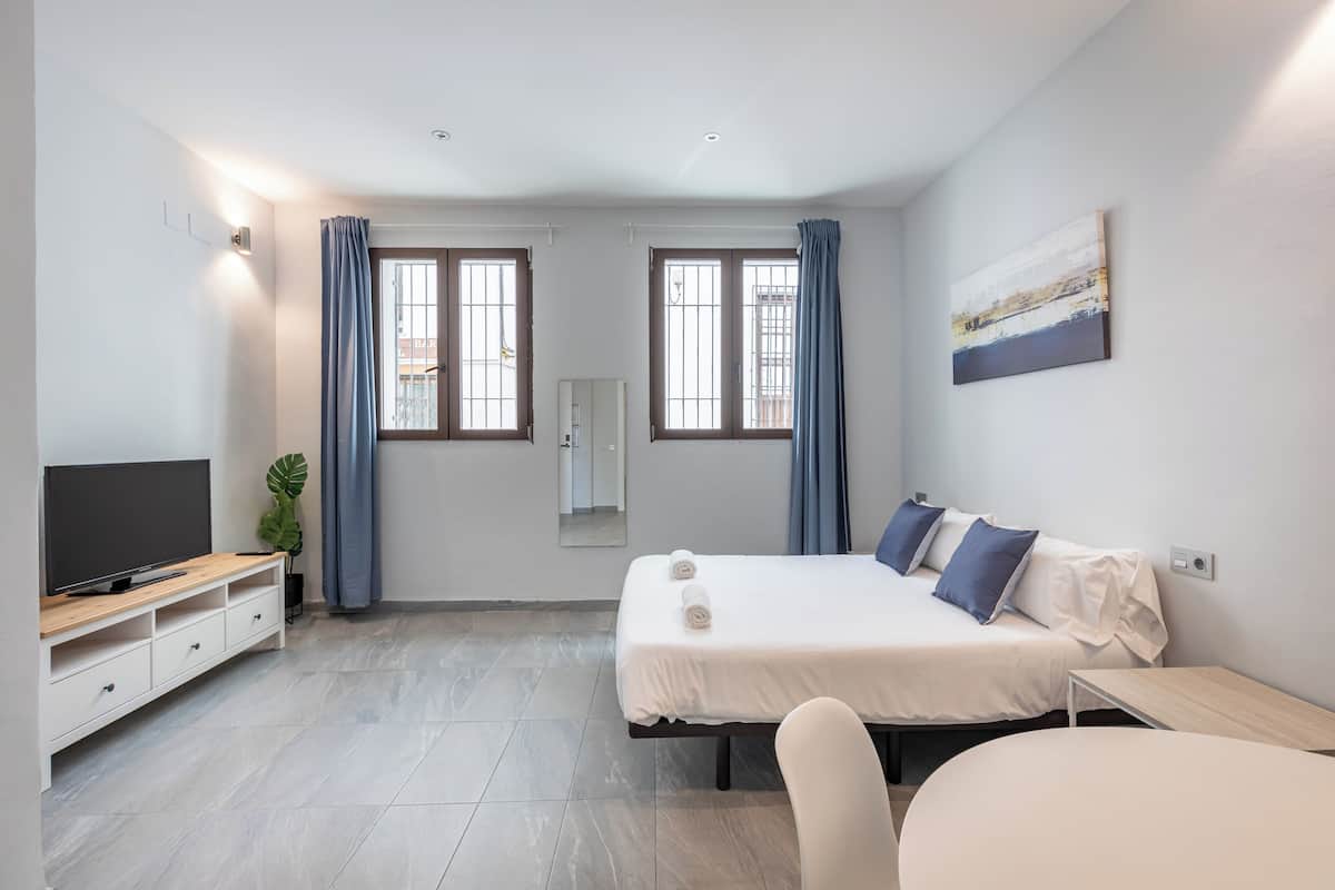 A modern hotel room with a bed, a TV, a desk, and a chair.