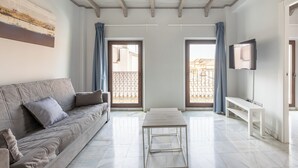 A spacious living room with a sofa, a coffee table, and a TV on a stand. There are two doors leading to a balcony. - Apartamentos Realejo Granada Centro 3000 (Granada)