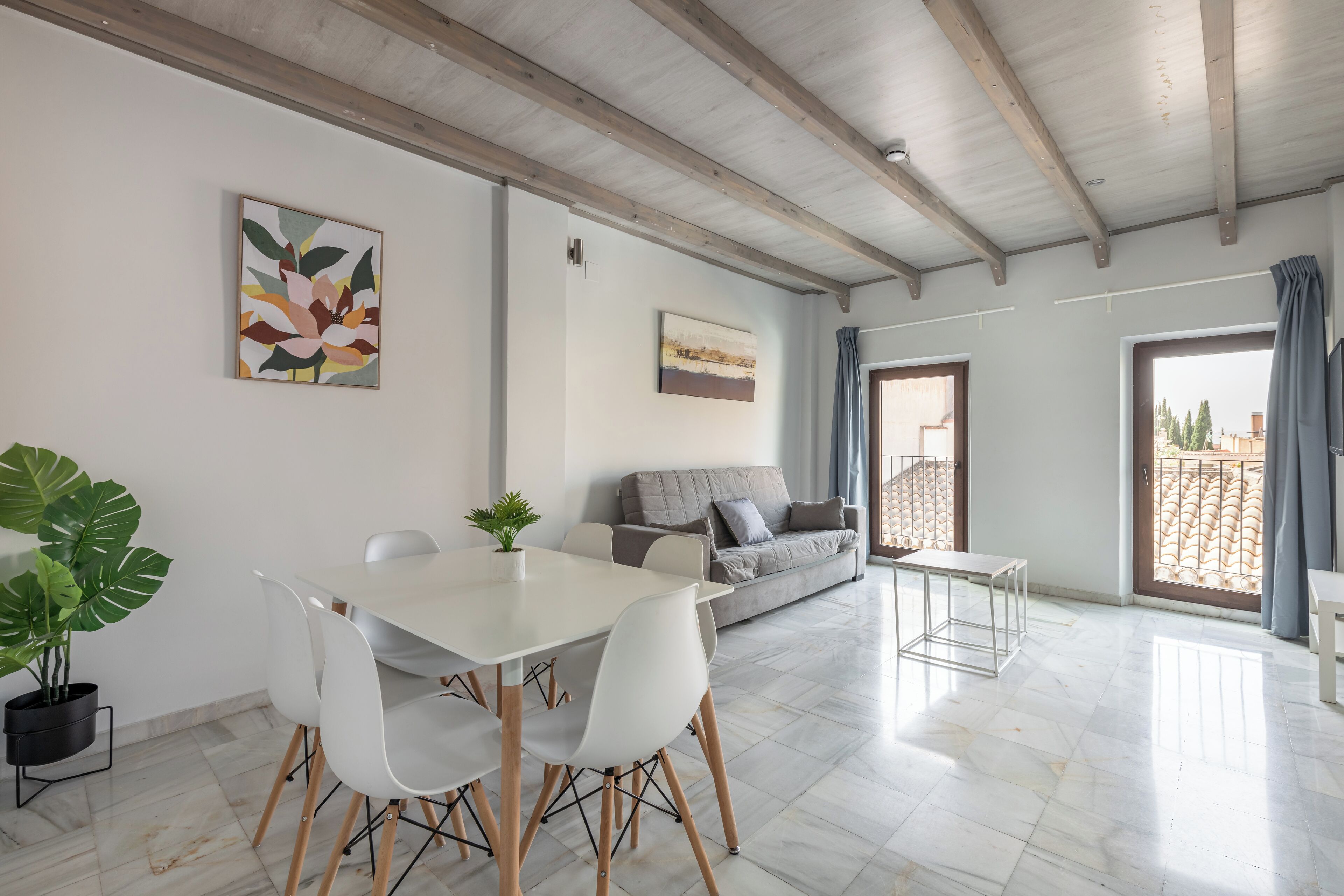 Una sala de estar moderna con una mesa de comedor, sillas blancas, un sofá gris y un ventanal con cortinas.
