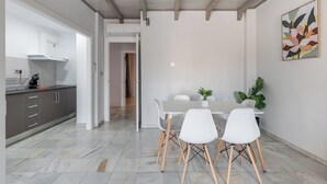 A modern kitchen with grey cabinets and a white countertop, a dining area with a white table and chairs, and a hallway leading to another room. - Apartamentos Realejo Granada Centro 3000 (Granada)
