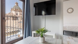 A room with a large window, a flat-screen TV mounted on the wall, a small potted plant on a table, a bed, and a white bedside table. - Apartamentos Realejo Granada Centro 3000 (Granada)