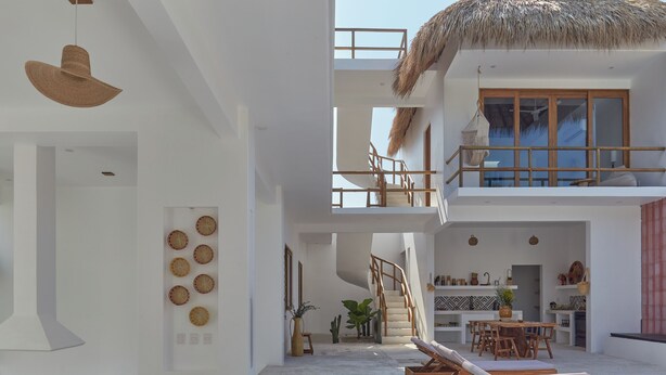 Una villa moderna de varios niveles con techo de paja, un comedor y un área de descanso junto a la piscina.