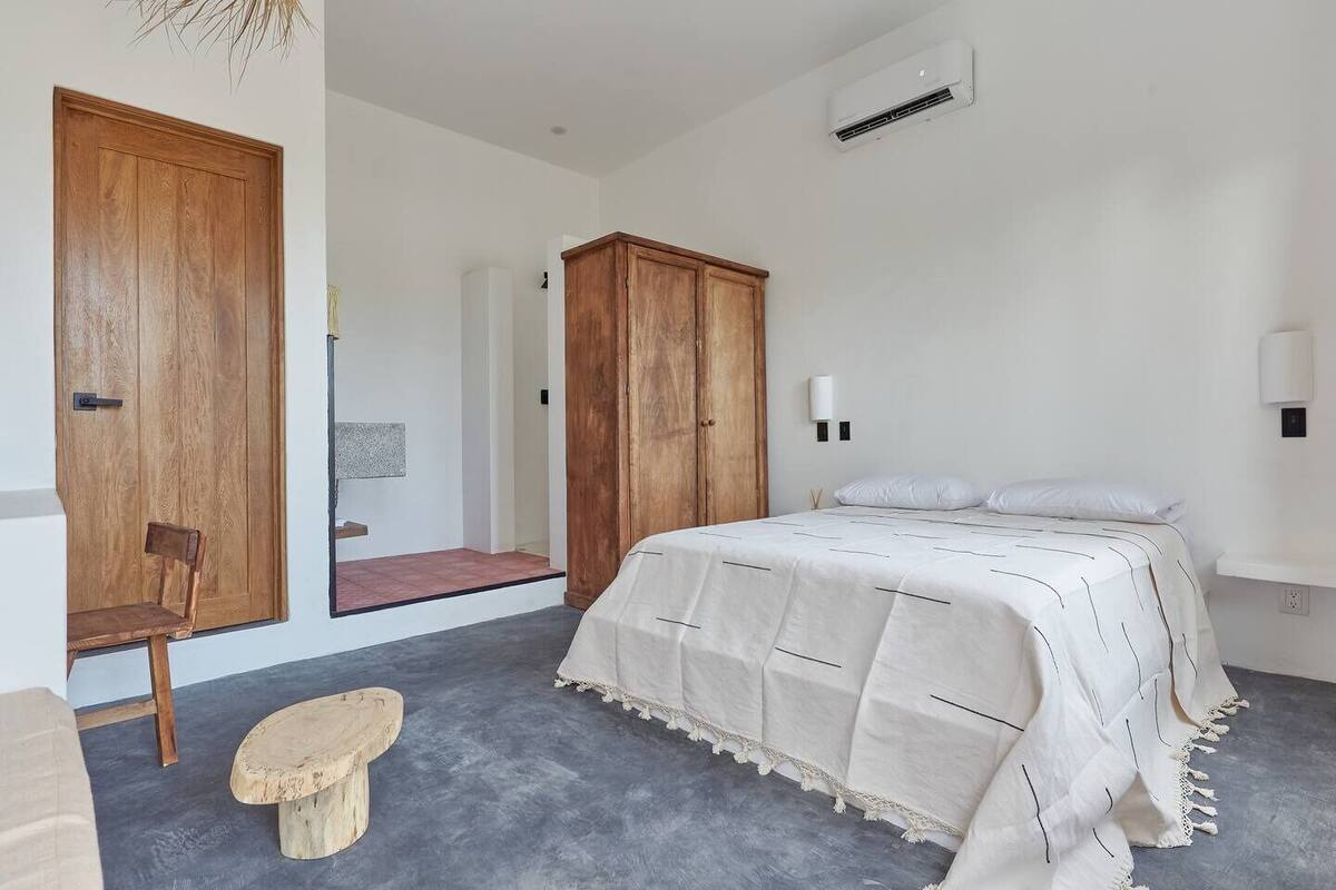 A bedroom with a bed, a wooden wardrobe, a chair, and a small stool.