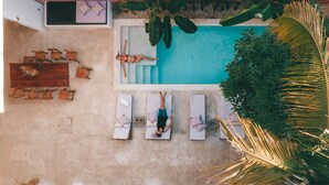 Vista aérea de una zona de piscina con sillas de descanso, una persona relajándose y vegetación circundante.
