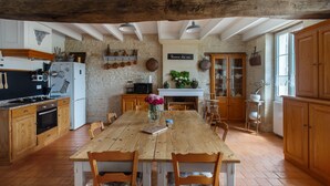 A rustic kitchen with wooden furniture, a dining table, and a stone wall. - Holiday Home “La Longère Claudine” with Shared Pool, Terrace & Wi-Fi (Fontenet)