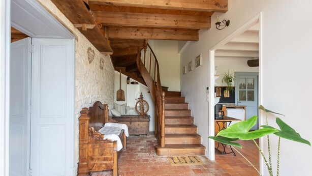 A rustic interior with a wooden staircase, a bed, a dresser, and a kitchen area. - Holiday Home “La Longère Claudine” with Shared Pool, Terrace & Wi-Fi (Fontenet)