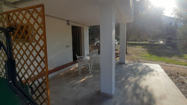 A covered outdoor area with a table and chairs, a wooden lattice partition, and a view of a park. - Vacation home 200 mt from the sea in sardinia (Tertenia)